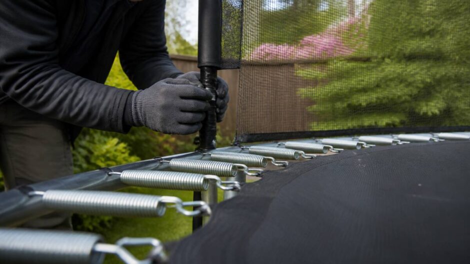 Iemand inspecteert de veiligheidsnet-bevestiging en springmat van een trampoline in de lente