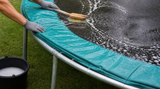 Iemand maakt de springmat, het randkussen en het frame van een trampoline schoon met een zachte borstel en mild sopje